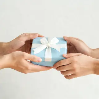 One person handing a small gift box to another person, both 