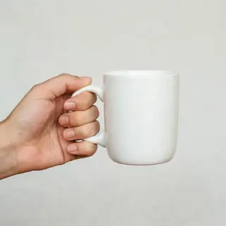 A person holding a white ceramic coffee mug by the handle wi
