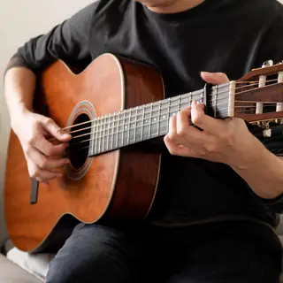 A person playing an acoustic guitar with left hand on the fr