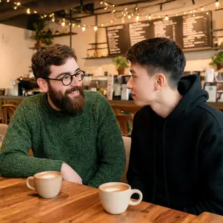 Two men at a cafe: one with a beard and glasses wearing a gr