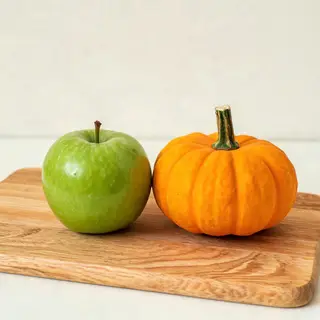 A green apple and an orange pumpkin on a wooden cutting boar