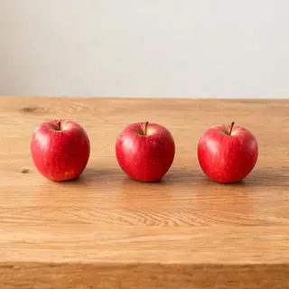 Exactly 3 red apples arranged on a wooden table