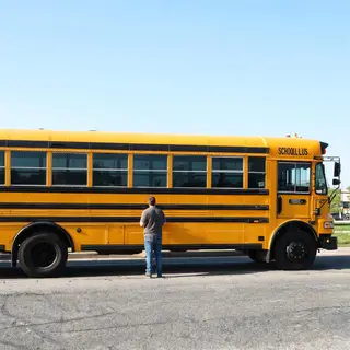 A person standing next to a yellow school bus, showing reali