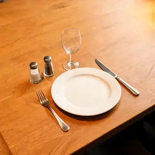 A dinner table scene with a plate, fork, knife, wine glass, 