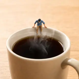 A tiny person standing on the rim of a coffee cup, looking d