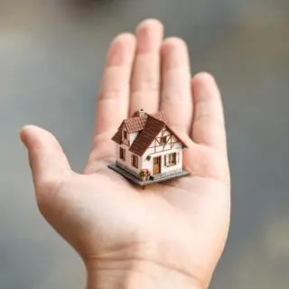A miniature house sitting on the palm of someone's hand