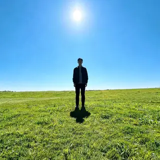 A person standing outdoors at midday with a short shadow dir