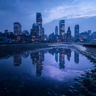 A city skyline reflected in a rain puddle on a street, with 