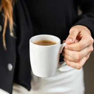 A person holding a white ceramic coffee mug by the handle wi