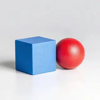 A red ball and a blue cube sitting side by side on a white s