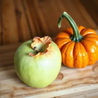 A green apple and an orange pumpkin on a wooden cutting boar