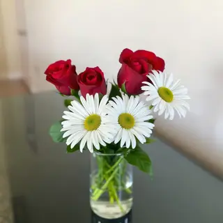 4 red roses and 2 white daisies in a glass vase on a table