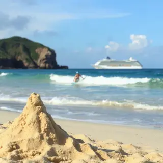A beach scene with a sandcastle in the foreground, a surfer 