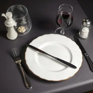 A dinner table scene with a plate, fork, knife, wine glass, 