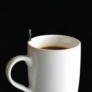 A tiny person standing on the rim of a coffee cup, looking d