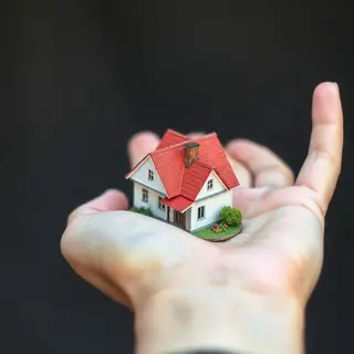 A miniature house sitting on the palm of someone's hand