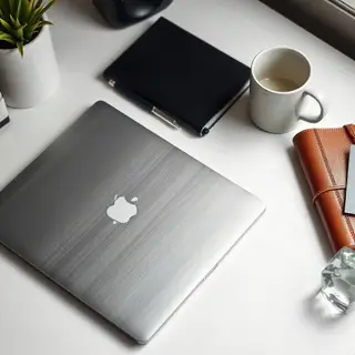 A workspace desk with a brushed aluminum laptop, a leather-b
