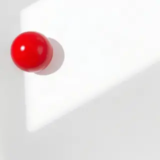 A red sphere on a white surface with a single shadow cast to