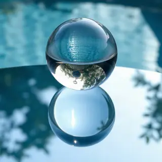 A clear glass sphere sitting on a mirror surface near a pool