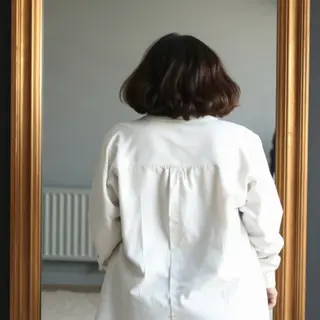 A woman standing in front of a full-length mirror, her refle