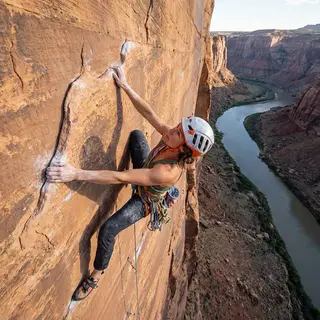 A rock climber clinging to a cliff face with arms and legs e