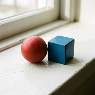 A red ball and a blue cube sitting side by side on a white s