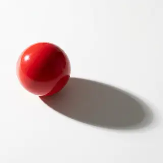 A red sphere on a white surface with a single shadow cast to
