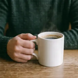 A person holding a white ceramic coffee mug by the handle wi