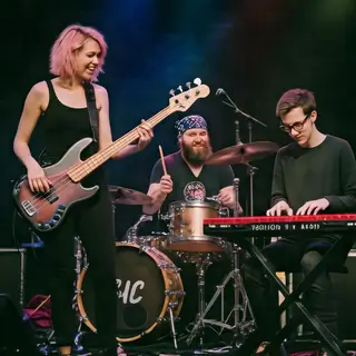 Three musicians on stage: a tall woman with short pink hair 