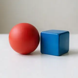 A red ball and a blue cube sitting side by side on a white s