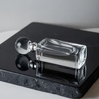 A clear glass perfume bottle on a reflective black surface w