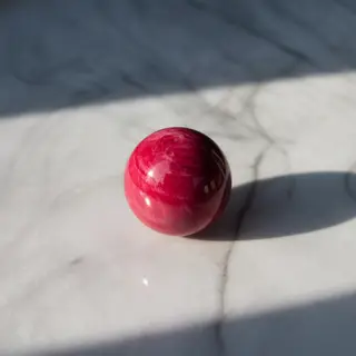 A red sphere on a white surface with a single shadow cast to