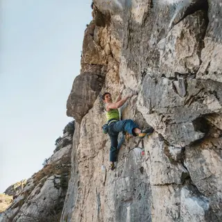 A rock climber clinging to a cliff face with arms and legs e