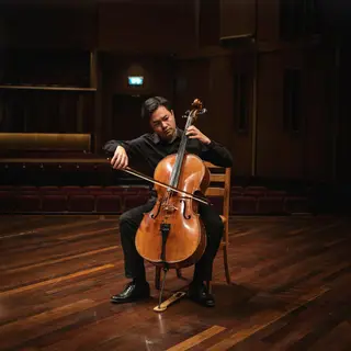 A cellist seated with correct posture, legs around the instr