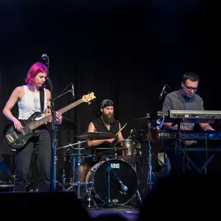 Three musicians on stage: a tall woman with short pink hair 