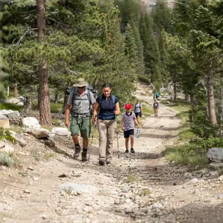 Three hikers on a trail: a man with a backpack and sunhat, a