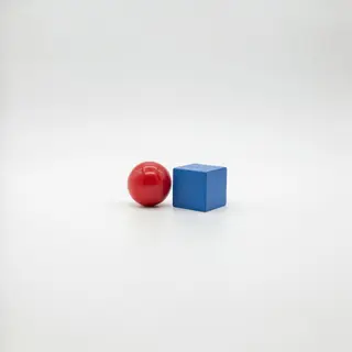 A red ball and a blue cube sitting side by side on a white s