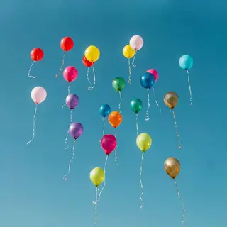 Exactly 11 colorful balloons floating against a clear blue s