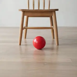 A red ball underneath a wooden chair