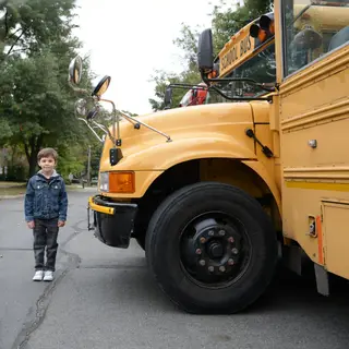 A person standing next to a yellow school bus, showing reali