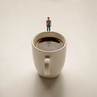 A tiny person standing on the rim of a coffee cup, looking d