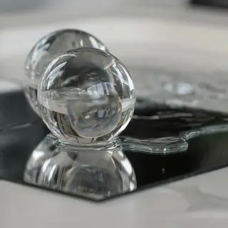 A clear glass sphere sitting on a mirror surface near a pool