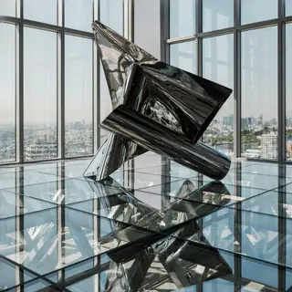 A chrome sculpture in a room with a glass floor and large wi