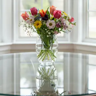 A vase of flowers on a glass table with a clear reflection v