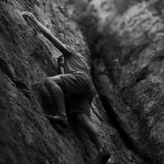 A rock climber clinging to a cliff face with arms and legs e