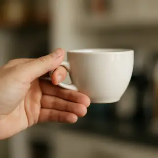 A person holding a white ceramic coffee mug by the handle wi