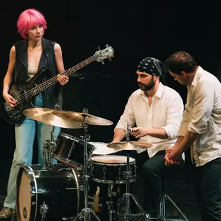 Three musicians on stage: a tall woman with short pink hair 