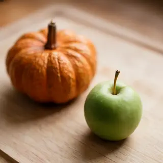 A green apple and an orange pumpkin on a wooden cutting boar