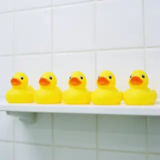 Exactly 5 yellow rubber ducks sitting in a row on a bathroom
