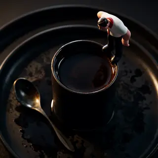 A tiny person standing on the rim of a coffee cup, looking d